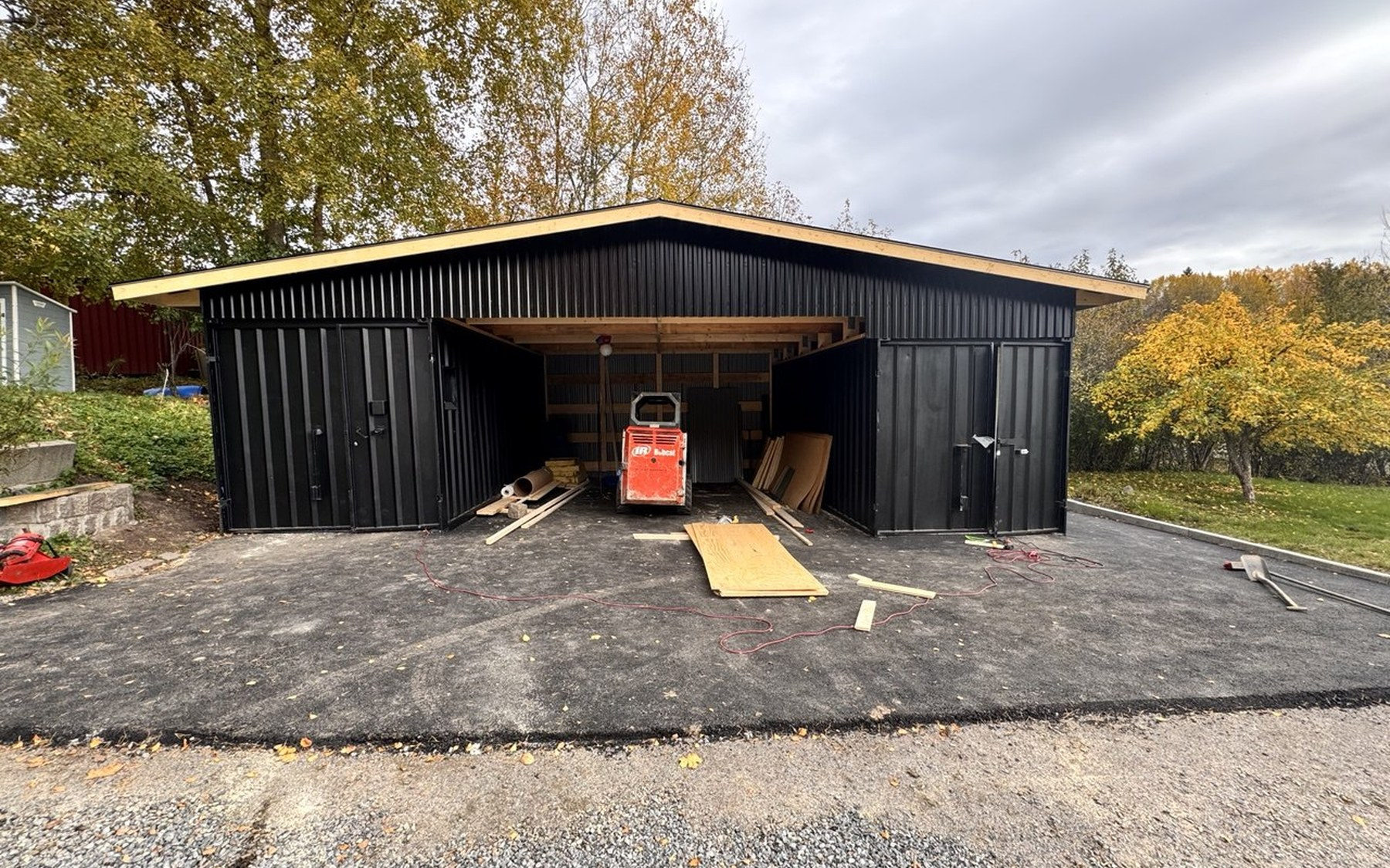 Stuvsta garage med två mörka förrådsvolymer och en skyddad carport