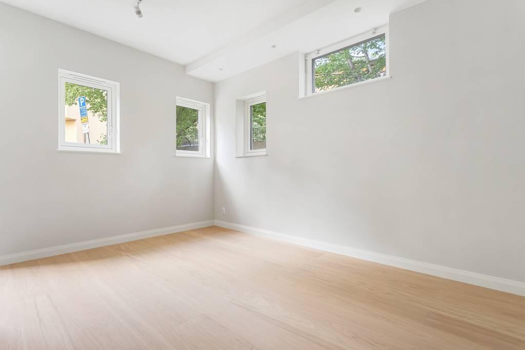 Ljust och luftigt allrum med flera högt sittande fönster som ger ett generöst ljusinsläpp över trägolvet.