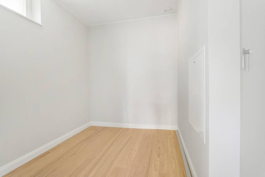 Tomt rum som visar mötet mellan det ljusa trägolvet och de vita väggarna.